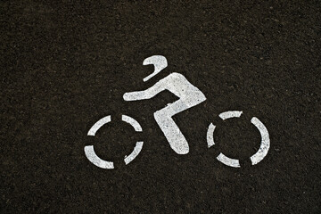 Outline of a biker in helmet, white paint on black tarmac / asphalt, centered.