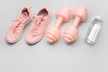 Dumbbells, shoes and bottle of water on light background