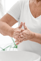Elderly woman washing hands in bathroom