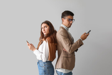 Quarreled young couple using mobile phones on light background