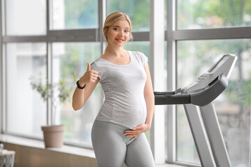 Young pregnant woman showing thumb-up in gym
