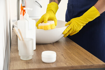 Young man with sponge cleaning sink in bathroom, closeup