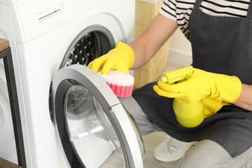Young man cleaning washing machine with sponge in bathroom, closeup
