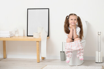 Little girl sitting on toilet bowl in bathroom