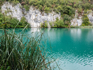 Bright blue color of lake against stone cliff in Plitvice Lakes District, Croatia. 