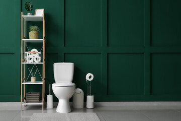 Interior of restroom with toilet bowl, shelving unit and green wall
