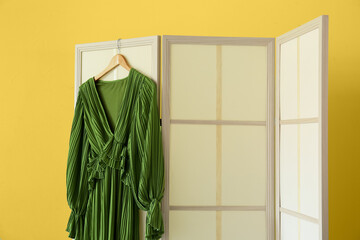Beige folding screen with beautiful dress near yellow wall
