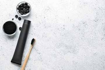 Toothpaste tube, bamboo toothbrush, bowls with activated charcoal tooth powder and pills on light background