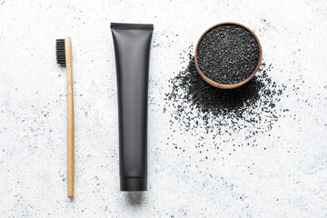 Bowl with activated charcoal tooth powder, toothpaste tube and bamboo toothbrush on light background