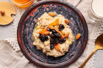 Delicious oatmeal covered with prunes, dried apricots, almond nuts and honey in plate on light table
