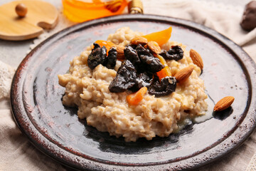 Delicious oatmeal covered with prunes, dried apricots, almond nuts and honey in plate on table, closeup
