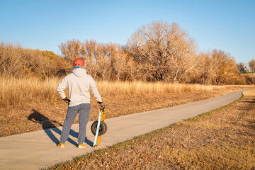senior man is standing with one-wheeled electric skateboard on a paved bike trail in fall scenery in Colorado