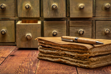 antique leather-bound journal or book with decked edge handmade paper pages and a stylish pen on a weathered barn wood table with rustic apothecary drawers