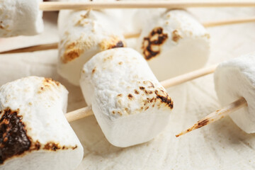 Skewers with tasty grilled marshmallows on light background, closeup