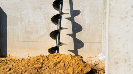 Gasoline drill for the ground on the background of a gray concrete wall with the ground in the...
