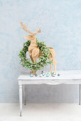 Wooden reindeer and Christmas wreath on white table near color wall
