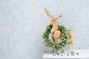 Wooden reindeer, Christmas wreath and balls on white table near color wall
