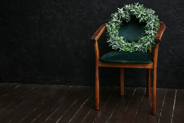 Armchair with Christmas wreath near dark wall