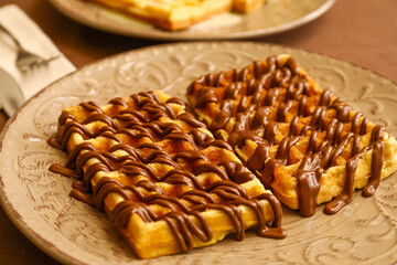 Plate of tasty Belgian Waffles with chocolate on table in cafe, closeup