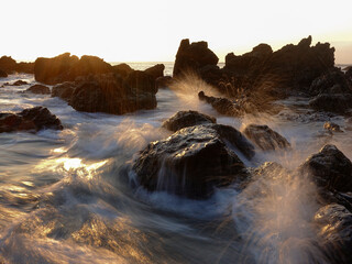 Motion effect, waves crashing rocks on the beach at sunset.