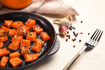 Frying pan with tasty roasted pumpkin pieces on light background