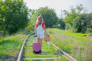 girl with a hat walking on the railroad with a suitcase