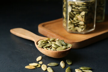 Spoon and jars with pumpkin seeds on black background