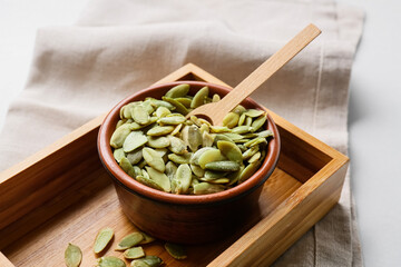Bowl with pumpkin seeds on light background
