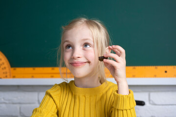 Close-up portrait of attractive small little cheerful girl sitting on table desktop in class room,...