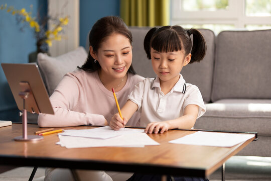Young Chinese mother helping daughter with her homework in living room