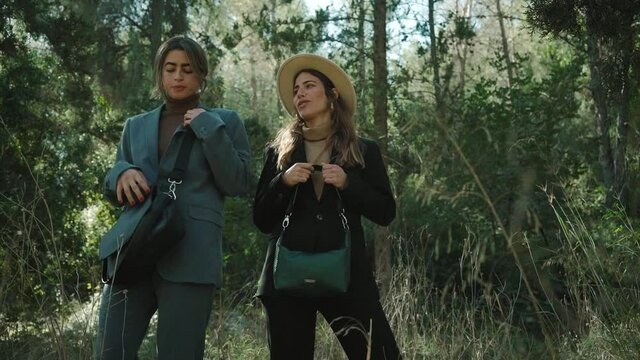 two beautiful women models talk to each other before posing for camera wearing trendy suits in a forest