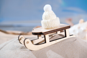 wooden toy sleigh on a sandy beach with small white hat. winter holiday travel to ocean or sea. exotic resort christmas and new year celebration