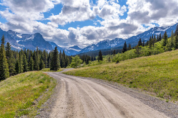 Spring Mountain Road - A dirt country road winding in Cut Bank Valley towards high peaks of Lewis...