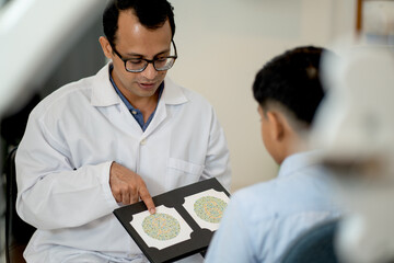 Indian optical staff point to page of book for testing color blindness to children during the process in optical shop.