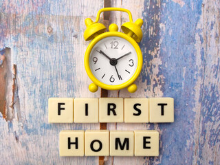 Toys word with text FIRST HOME with clock on a wooden background.
