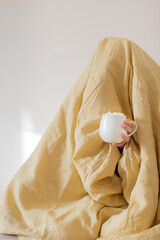 Woman under a yellow blanket with his head. A mug with marshmallows and a drink is on display outside. The concept of autumn and winter.