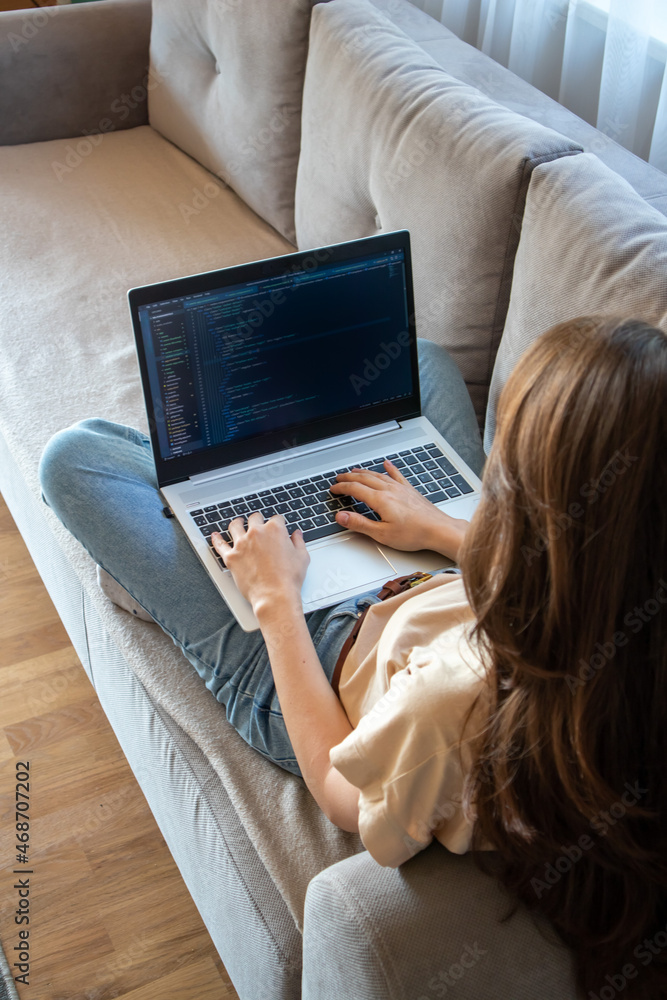 Wall mural woman working on a laptop while sitting on the sofa. a girl programmer is coding