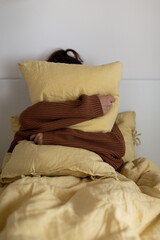 The girl hugs a yellow pillow sitting in bed in a warm sweater. The concept of autumn and winter.