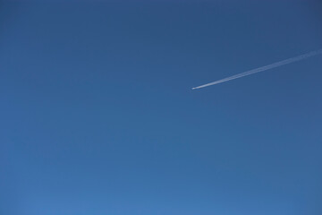 White contrail from an airplane in a clear blue sky.