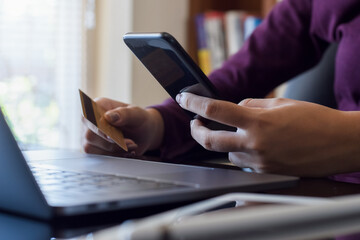 Fototapeta premium Online shopping and credit card payment concept. Young woman hands holding credit card and using mobile smart for electronic banking at home.