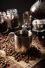 Metallic cup and vacuum coffee maker also known as vac pot, siphon or syphon coffee maker and toasted coffee beans on rustic wooden table