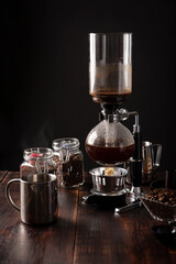 Vacuum coffee maker also known as vac pot, siphon or syphon coffee maker. Metallic cup and toasted coffee beans on rustic wooden table