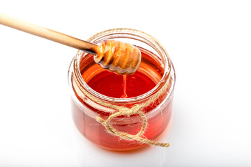honey in a clear glass jar There is a wooden dipper that stirs honey and drops honey.isolated on white background.