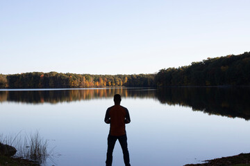 Fototapeta na wymiar A person standing on the calm lake with fall colors. 