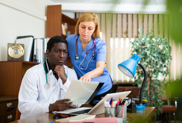 Obraz premium Two focused professional doctors working at table in office of clinic, discussing medical histories of patients