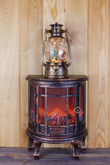 Decorative electric fireplace against a wooden wall with a lamp on the shelf. Santa Claus is standing inside the lamp, a Christmas tree and silver snowflakes are spinning. Christmas landscape.