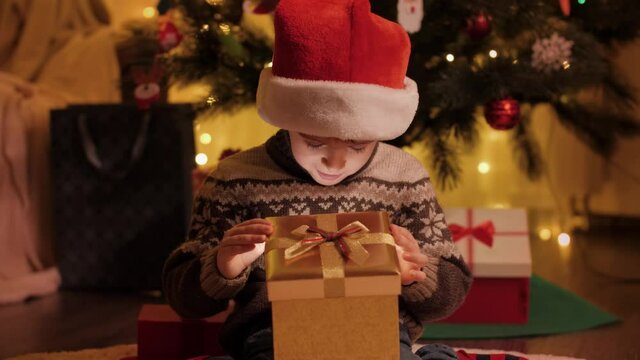 Cute boy in Santa hat looking inside Christmas present box. Christmas holiday magic. Families and children celebrating winter holidays.