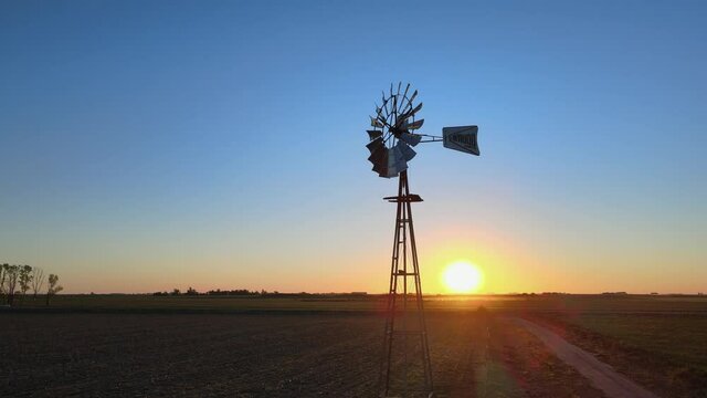 Cinematic vintage pan shot around old antique windmill on an open agriculture field in rural countryside at sunset, La Pampa, Patagonia, Argentina.