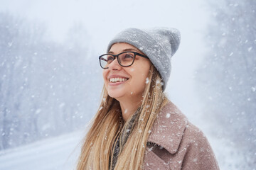 Portrait of a blonde woman in glasses and a gray hat, rejoices in the first snow in winter