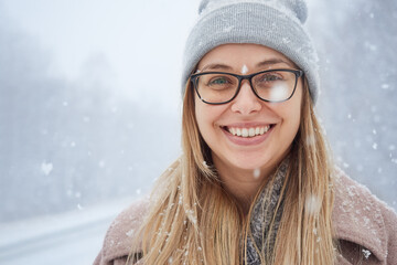 Close-up portrait of happy young woman in park during snowfall in winter